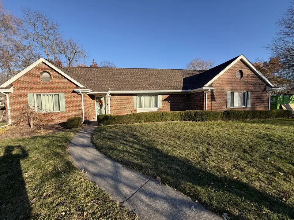 Long brick ranch home with a dark shingle roof and a curved front walk.