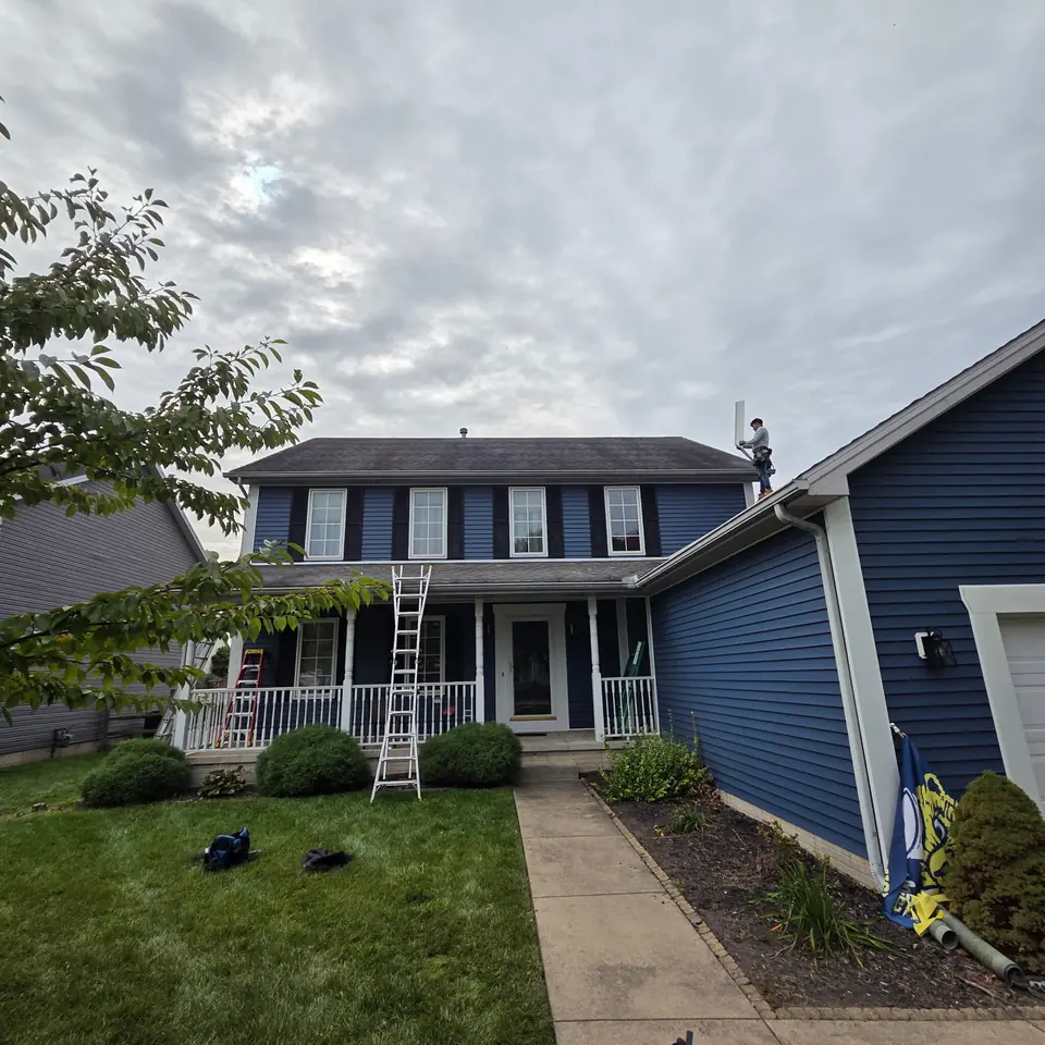 Blue siding and white gutters on a two-story home, with an installer working at the roofline.