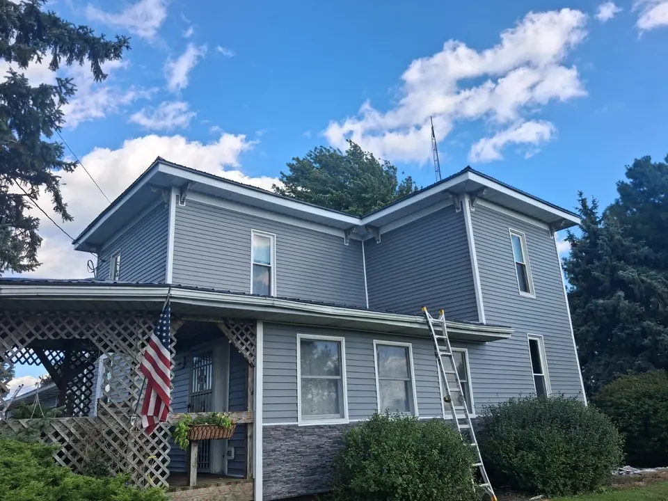 Gray siding and white trim on a two-story farmhouse with a covered porch and stone base.