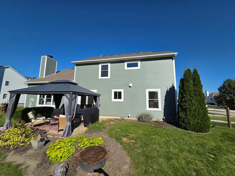 Sage green siding across the back of a two-story home, with a gazebo and patio in the yard.