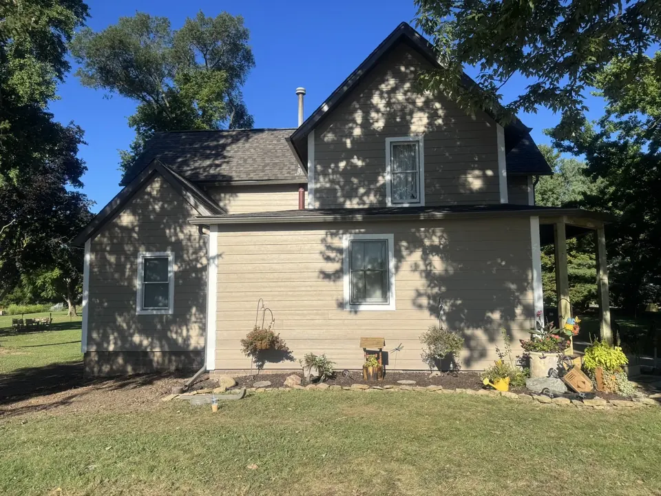 Two-story home with light tan siding on a sunny day, seen from the side yard.